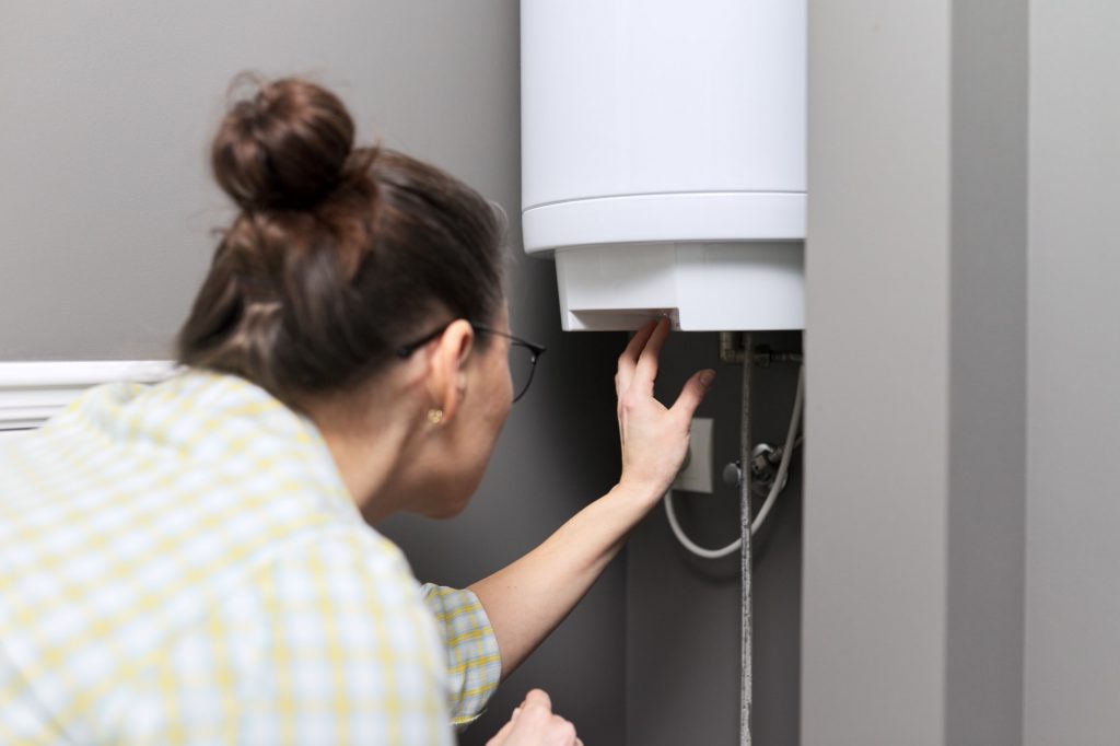 Home water heater, woman regulates the temperature on an electric water heater